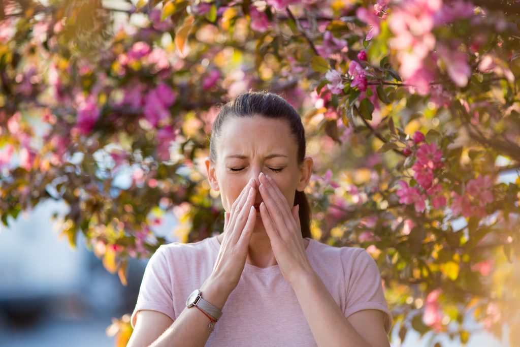 Young women stopped to sneeze as she walked by a tree during spring.