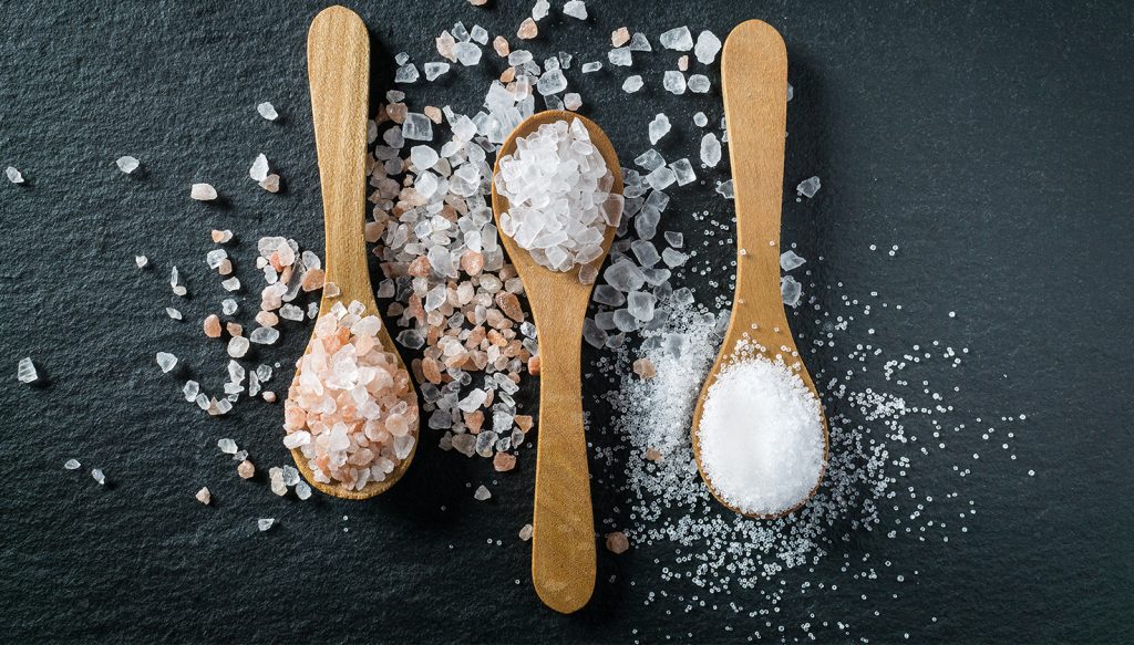 Three wooden spoons with fine salt, white salt rocks, and pink salt rocks.