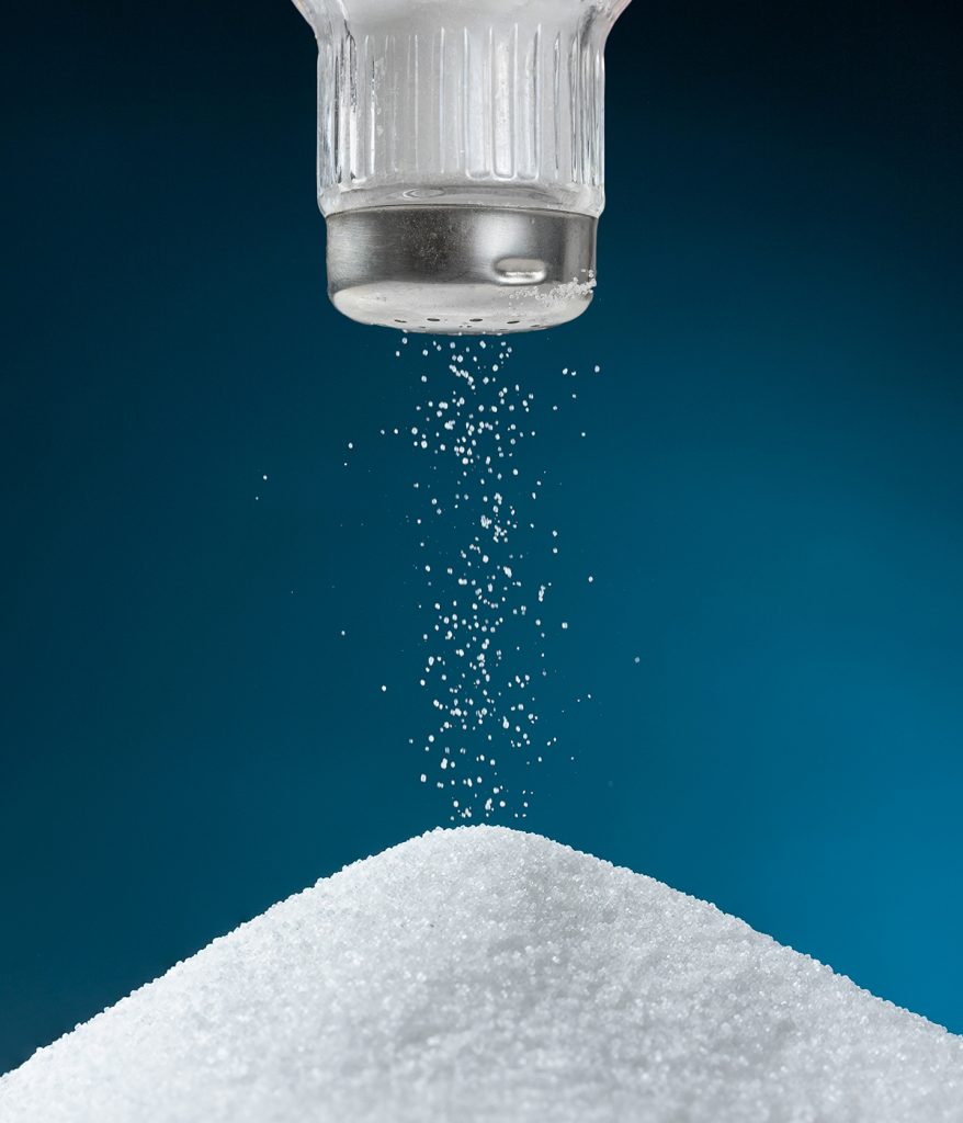 Salt shaker dropping salt in a pile of granulated salt.