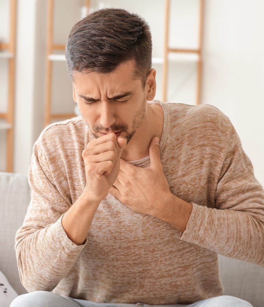 Young man coughing as he holds his chest.