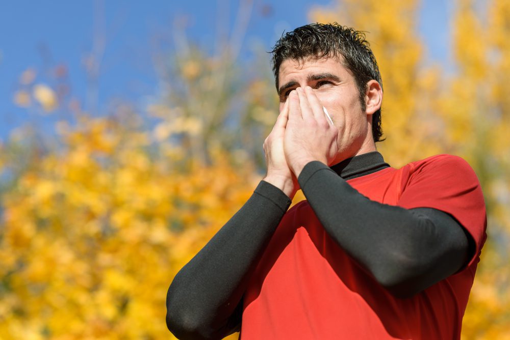 Middle aged man sneezing into tissue as he exercises outside.