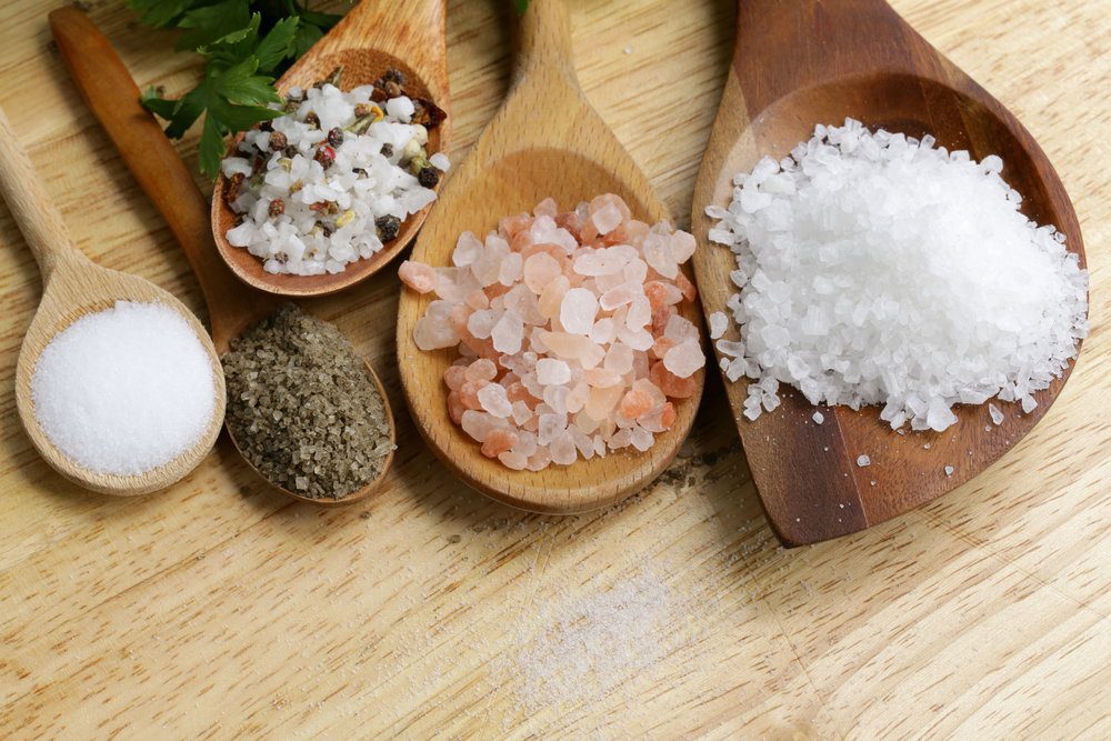Five wooden spoons of different sizes with a variety of salts.