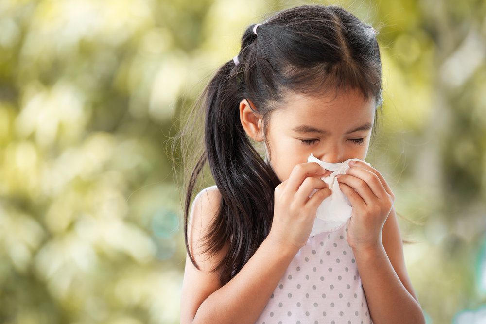 Asian little girl sneezing into tissue.