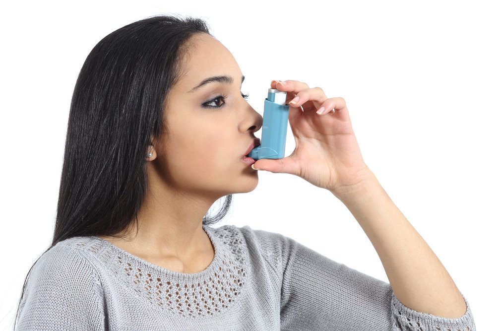 Head shot of an Indian woman using an inhaler.