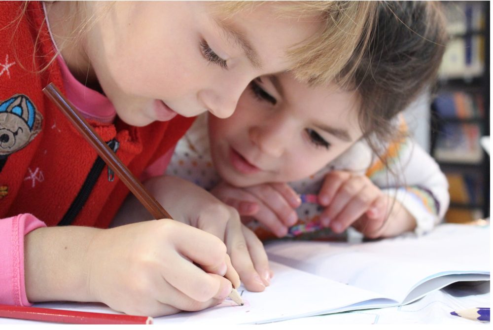 Two little girls side by side at school drawing a picture.