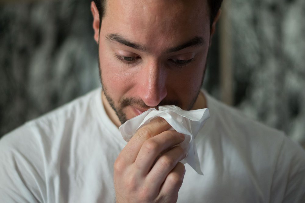 Middle aged man wiping nose with tissue.