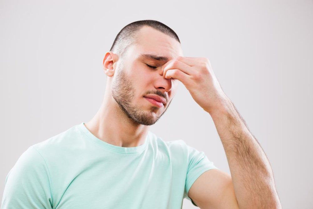Young man with headache and sinusitis applying pressure on nose and sinus areas.