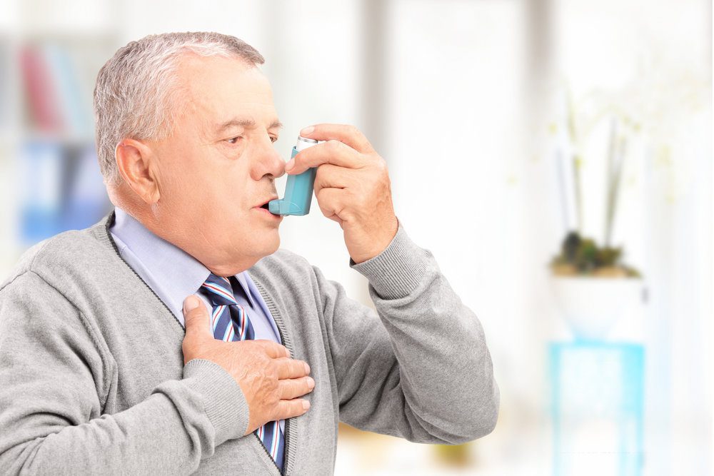 Older white man using an inhaler.
