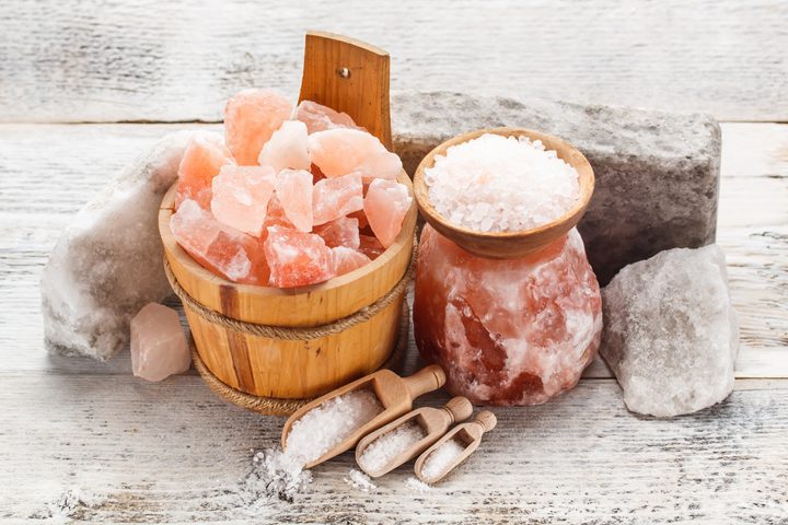Himalayan pink salt rocks in wooden container, crushed salt in wooden spoons and small bowl.