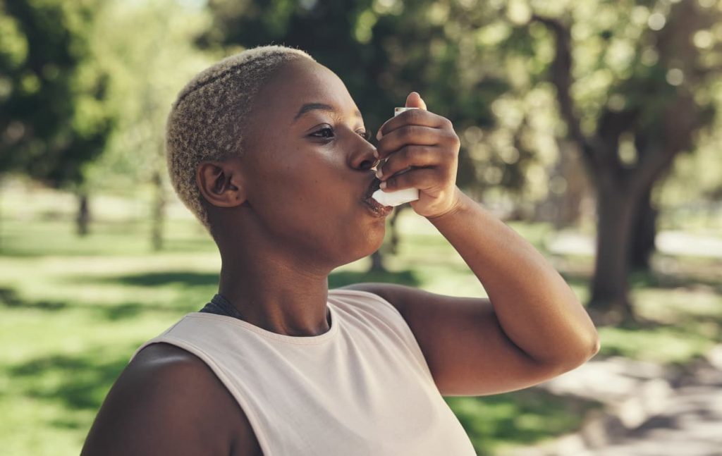 A woman with asthma breathing with an inhaler outside