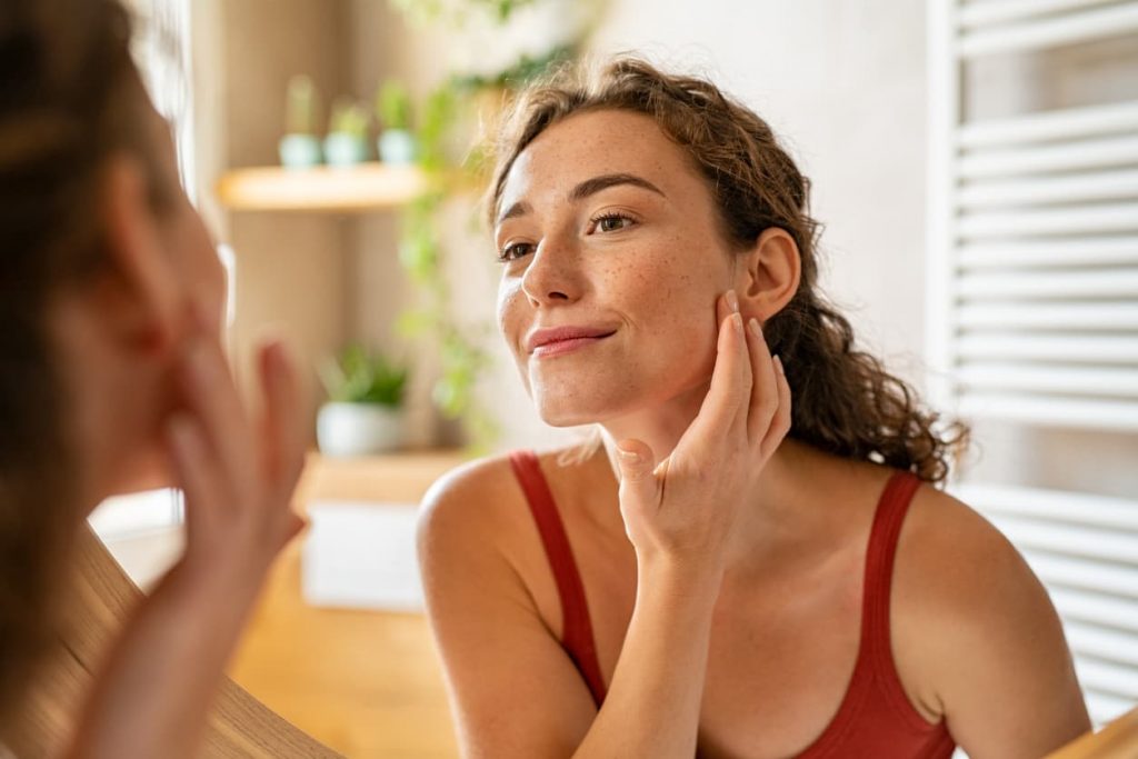 A woman examining her skin for aging and eczema in the mirror